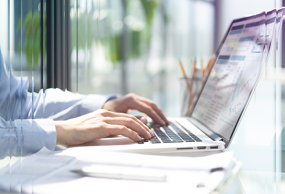 Hands typing on laptop with analytics on screen